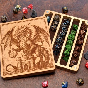 May include: A rectangular wooden dice storage box with a laser-engraved dragon and castle design on the lid. The open box features four long, velvet-lined channels containing various multi-sided dice in green, black, and metallic finishes.