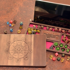 Op de afbeelding: Een houten speldoos met een lasergegraveerd kompasontwerp op het deksel. De open binnenzijde is voorzien van een magenta viltvoering, meerdere vakken voor veelzijdige dobbelstenen, een Daggerheart-logo en een gleuf voor een tablet.