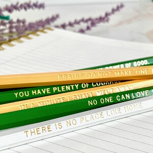 May include: Close-up of several pencils with gold lettering. The pencils are in various colors, including green, natural wood, and white. The text on the pencils includes inspirational quotes such as "Brains do not make one", and "There is no place like home".