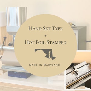 May include: A close-up of a hot foil stamping machine with a hand set type. The machine is made in Maryland and features a gold circle with the text "HAND SET TYPE + HOT FOIL STAMPED" and a black outline of the state of Maryland.
