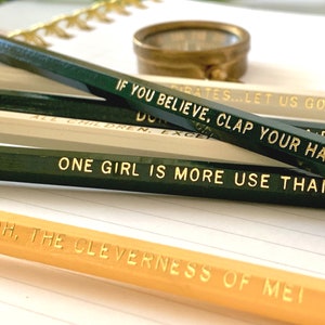 Puede incluir: Primer plano de cuatro l&aacute;pices con barriles pintados de verde y blanco y letras doradas. Los l&aacute;pices tienen el siguiente texto: "Pirates... Let us go", "If you believe, clap your hands", "Don't all children, except", y "One girl is more use than", y "Oh, the cleverness of me!"