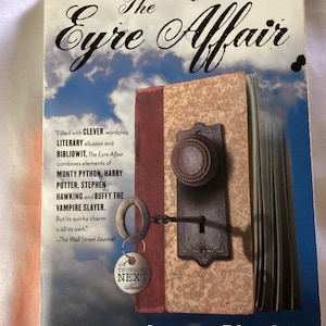 May include: A book cover with a blue sky background and a closed book with a key in the lock. The title of the book is "The Eyre Affair" and the author is "Jasper Fforde".