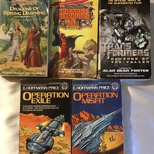 May include: A collection of nine paperback books, including fantasy novels like "Dragons of Spring Dawning" and "Wizards Warriors & You", a science fiction novel titled "Operation Exile", and a Transformers novel titled "Revenge of the Fallen".