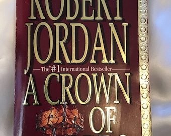 May include: A book cover with a burgundy background and gold lettering. The title is "A Crown of Swords" by Robert Jordan. The book is described as "The #1 International Bestseller".
