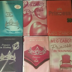 May include: Six paperback books in a series titled "The Princess Diaries" by Meg Cabot. The covers feature a pink, blue, and purple color scheme with crowns, hearts, and a throne.