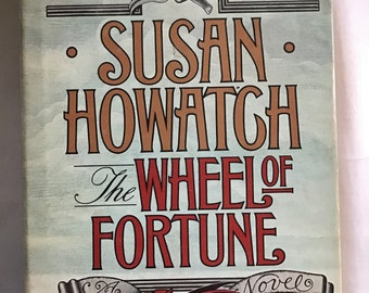 May include: A vintage book cover for "The Wheel of Fortune" by Susan Howatch. The cover features a red dragon, an angel, and the title in bold, decorative lettering. The background is a light blue with a landscape.