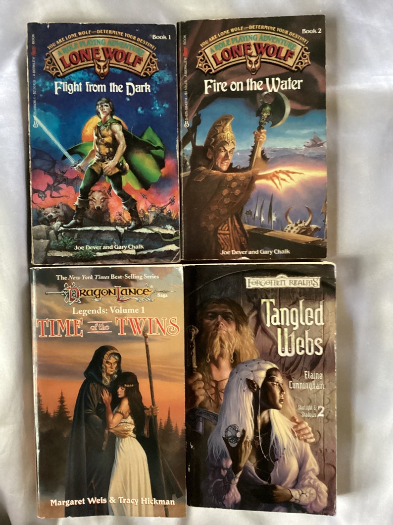 May include: Four fantasy novel covers. The first two are from the Lone Wolf series, titled "Flight from the Dark" and "Fire on the Water". The third is from the Dragonlance series, titled "Time of the Twins". The fourth is from the Forgotten Realms series, titled "Tangled Webs".
