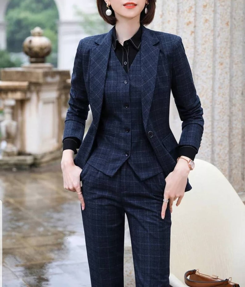 May include: A navy blue plaid pantsuit with a matching vest. The jacket has a notched collar and a single button closure. The pants have a straight leg.
