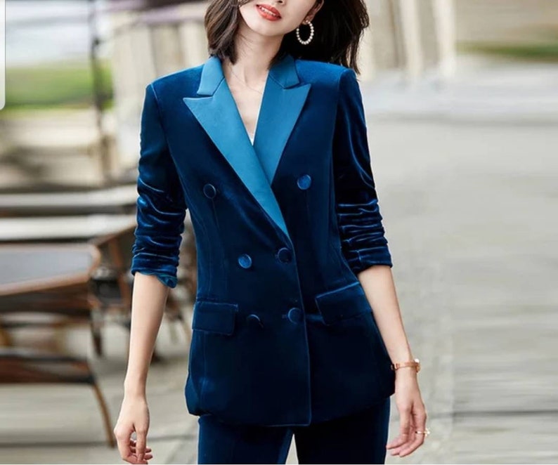 May include: A navy blue velvet blazer with a contrasting light blue lapel and buttons. The double-breasted jacket has long sleeves and a tailored fit, suggesting a formal or business attire style.