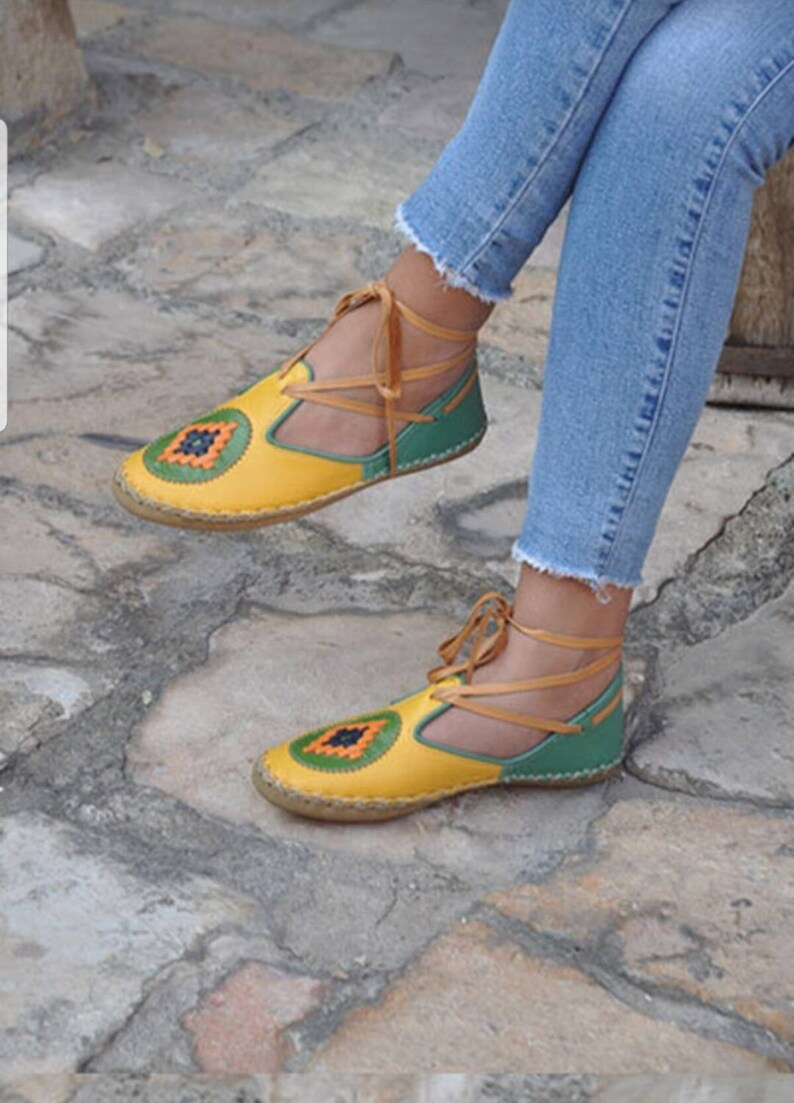 Puede incluir: Sandalias de cuero amarillas y verdes con un dise&ntilde;o decorativo en la puntera. Las sandalias tienen un dise&ntilde;o con cordones con cordones de color beige. Las sandalias se usan con vaqueros azules.
