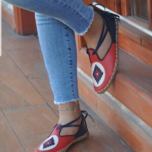 Puede incluir: Sandalias de cuero rojas y azul marino con un dise&ntilde;o geom&eacute;trico decorativo en la puntera. Las sandalias tienen una correa que se ata alrededor del tobillo. Las suelas son de color marr&oacute;n claro.
