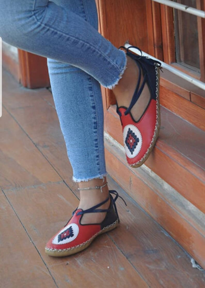 Puede incluir: Sandalias de cuero rojas y azul marino con un dise&ntilde;o geom&eacute;trico decorativo en la puntera. Las sandalias tienen una correa que se ata alrededor del tobillo. Las suelas son de color marr&oacute;n claro.