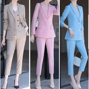 K&ouml;nnte beinhalten: Drei Frauen tragen passende Hosenanz&uuml;ge in verschiedenen Farben: Beige, Rosa und Hellblau. Jeder Anzug besteht aus einem Blazer mit einem einzigen Knopfverschluss und einer passenden Hose.