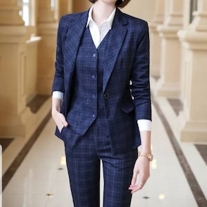 May include: A navy blue plaid blazer with a matching vest and pants. The blazer has a notched lapel and a single button closure. The vest has a V-neck and four buttons. The pants have a straight leg.