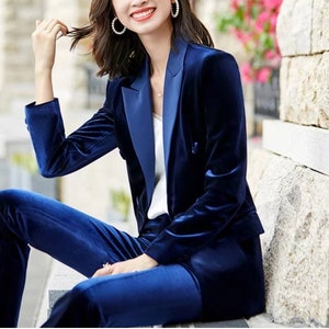 May include: A navy blue velvet suit, featuring a double-breasted blazer and matching trousers. The blazer has a satin lapel and the suit is tailored for a sleek, sophisticated look. The suit is a classic style.