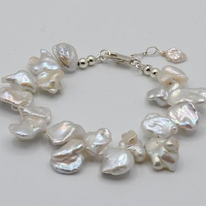 May include: A white pearl bracelet with an ornate silver clasp. The bracelet features irregularly shaped, lustrous white pearls. The pearls are strung together with a silver chain and clasp, creating a delicate and elegant piece of jewelry.
