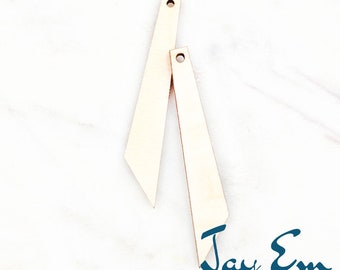 May include: Two unfinished wooden pieces with a hole at the top, each measuring 5 cm in length. The pieces are shaped like a long, thin triangle. The pieces are on a white marble surface. The text "Jay Em Laser Designs" is at the bottom of the image.