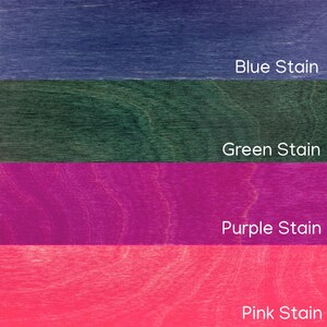 May include: A close-up of four wood samples stained in different colors. The top sample is blue, followed by green, purple, and pink. Each sample has the color name printed on it: Blue Stain, Green Stain, Purple Stain, and Pink Stain.