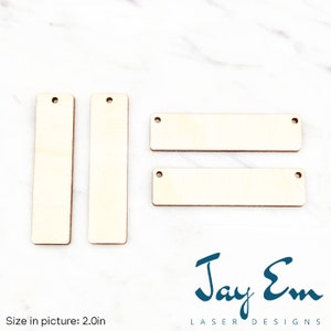 May include: Four unfinished wooden rectangular tags with holes for hanging. The tags are 2 inches long. The tags are on a white marble surface.