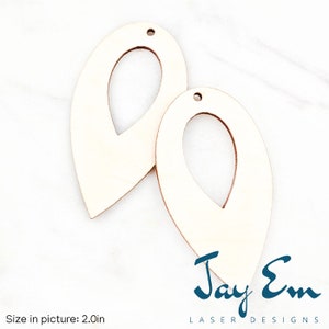 May include: Two unfinished wooden teardrop-shaped earrings with a hole at the top and a smaller hole in the center. The earrings are 2 inches in size.