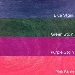 Pu&ograve; includere: Primo piano di quattro campioni di legno tinti in diversi colori. I colori sono blu, verde, viola e rosa. Ogni campione ha il nome del colore stampato in testo bianco: Blue Stain, Green Stain, Purple Stain e Pink Stain.