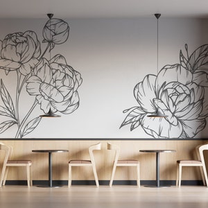 May include: A minimalist dining area with four chairs and two round tables. The walls are decorated with a black and white floral design. The chairs are made of light wood and have a simple design. The tables are also made of light wood and have a black metal base.