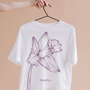 May include: White t-shirt with a purple line drawing of a flower and the text "beauty..." printed on the front.