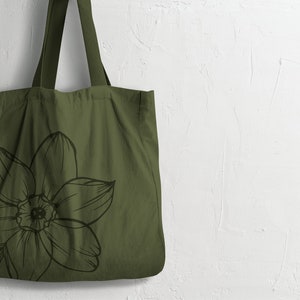 May include: A green canvas tote bag with a black and white floral design. The bag has two long handles.