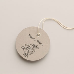 May include: A round, brown paper tag with a white string attached. The tag has a black and white illustration of a peony flower and the text "Peony Wear".