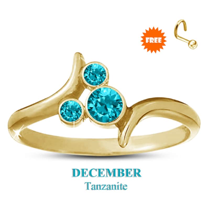 May include: A gold-colored ring with three round, bright blue tanzanite stones. The ring has a unique, flowing design. The word "DECEMBER" and "Tanzanite" are displayed in light blue text below the ring. A free nose ring is included.