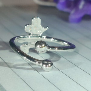 K&ouml;nnte beinhalten: Verstellbarer Ring in Silber mit einem kronenartigen Design. Der Ring hat zwei kugelf&ouml;rmige Enden. Das Metall ist gl&auml;nzend und reflektierend. Modeschmuck.