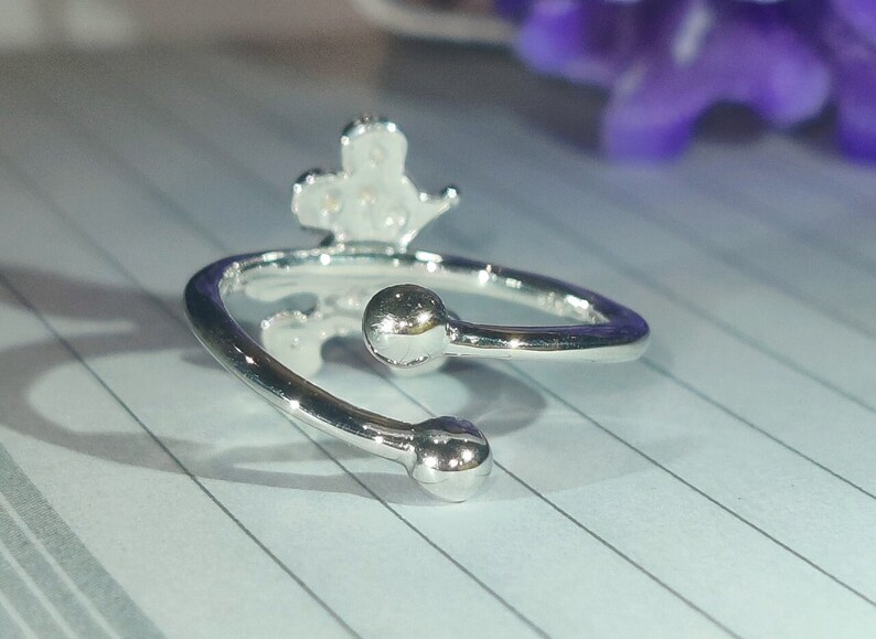 K&ouml;nnte beinhalten: Verstellbarer Ring in Silber mit einem kronenartigen Design. Der Ring hat zwei kugelf&ouml;rmige Enden. Das Metall ist gl&auml;nzend und reflektierend. Modeschmuck.