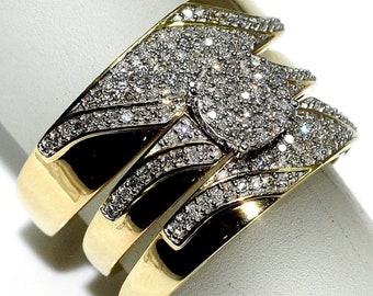 Könnte beinhalten: Dreiteiliges, goldfarbenes Ring-Set mit einem zentralen Cluster aus kleinen, funkelnden Steinen. Die Ringe haben ein breites Banddesign mit schwarzen Akzenten und zusätzlichen Steinen an den Rändern, was einen luxuriösen Look erzeugt.