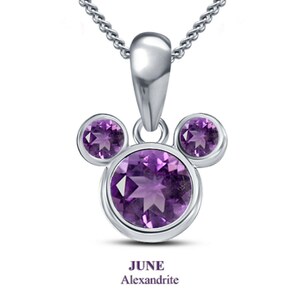 K&ouml;nnte beinhalten: Eine silberne Halskette mit Anh&auml;nger im Mickey-Mouse-Design, besetzt mit drei lila Edelsteinen. Der Anh&auml;nger hat einen gro&szlig;en Mittelstein und zwei kleinere Steine. Der Text "JUNE Alexandrite" steht darunter.