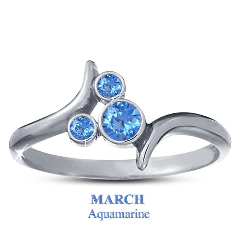 Puede incluir: Anillo de plata con tres gemas redondas de aguamarina azul claro. El anillo tiene un dise&ntilde;o &uacute;nico y fluido. El texto "MARZO" y "Aguamarina" en azul se encuentra en la parte inferior.