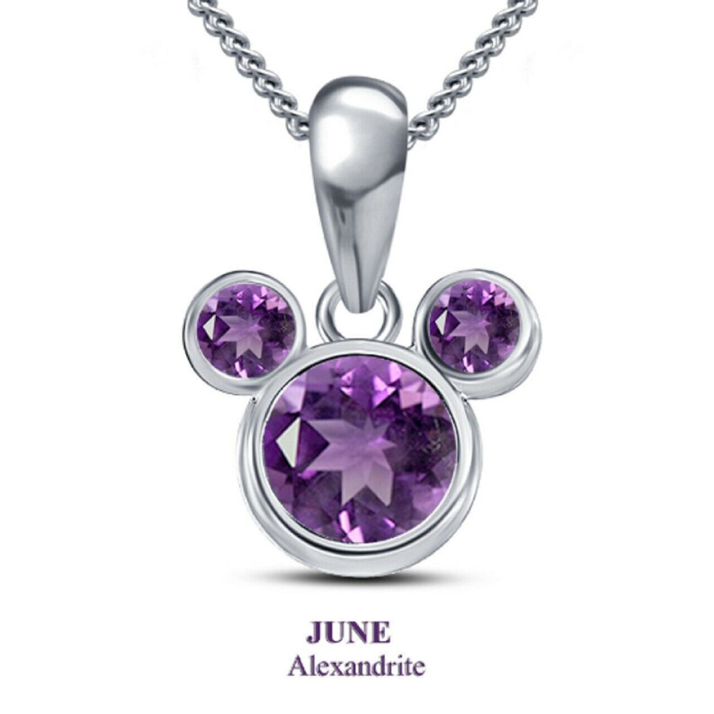 K&ouml;nnte beinhalten: Eine silberne Halskette mit Anh&auml;nger im Mickey Mouse-Design, besetzt mit drei runden, lila Edelsteinen. Der Anh&auml;nger h&auml;ngt an einer zarten Kette. Der Text "JUNE Alexandrite" befindet sich unten.