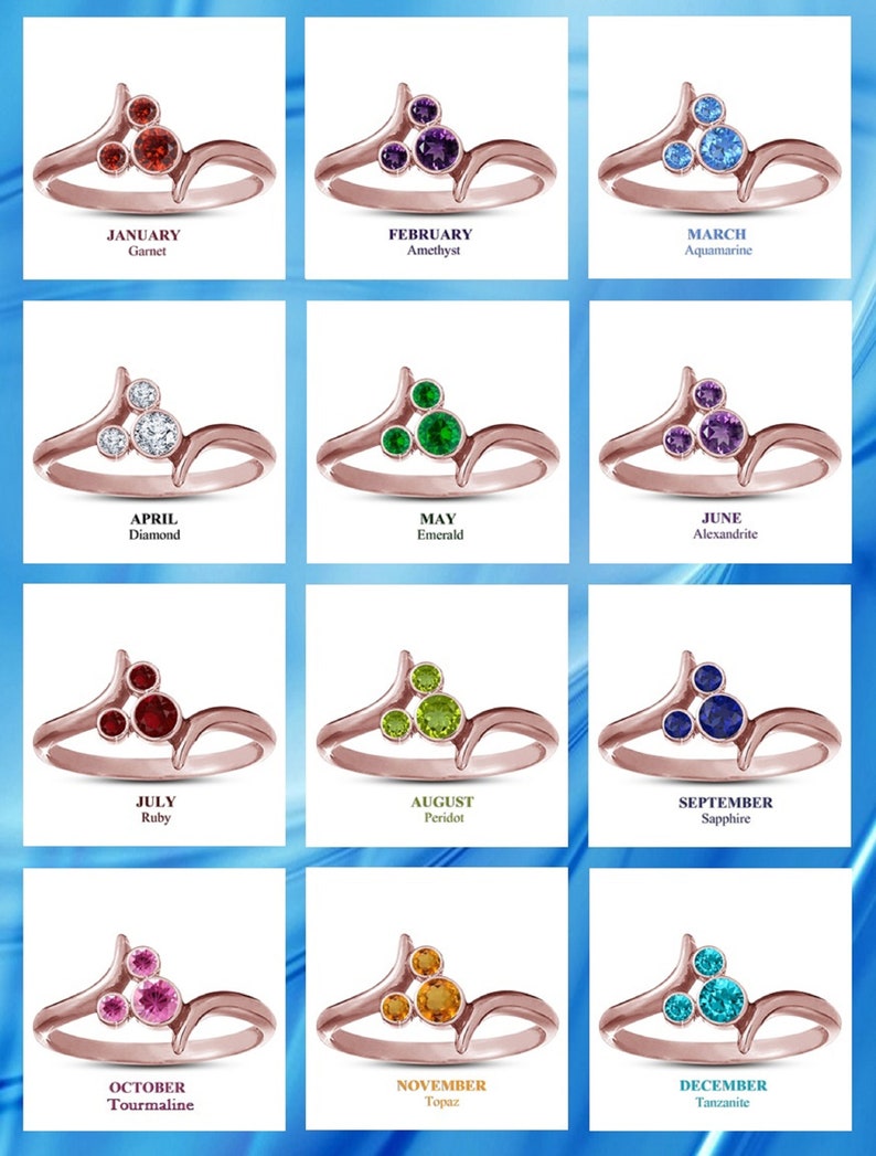 May include: A collection of rose gold rings, each featuring a cluster of gemstones. The rings are labeled with months and corresponding birthstones: Garnet, Amethyst, Aquamarine, Diamond, Emerald, Alexandrite, Ruby, Peridot, Sapphire, Tourmaline, Topaz, and Tanzanite.
