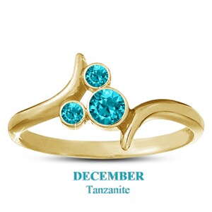 May include: A gold-colored ring with three round, bright blue gemstones. The ring has a unique, flowing design with the text "DECEMBER Tanzanite" below the ring.