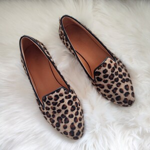 May include: A pair of leopard print flats with black trim. The shoes have a pointed toe and a flat heel.