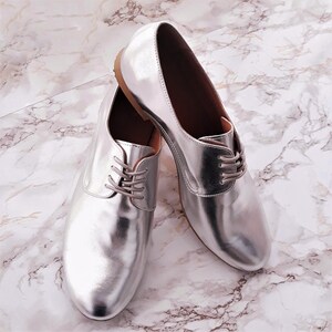 May include: A pair of silver leather lace-up shoes with a pointed toe.