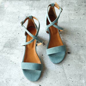 May include: A pair of light blue suede sandals with criss-cross straps and a low heel.