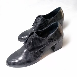 May include: A pair of black, textured leather shoes with a snakeskin pattern. The shoes have a lace-up design and a block heel. The heels are approximately 2.5 inches high.