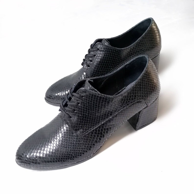 May include: A pair of black, textured leather shoes with a snakeskin pattern. The shoes have a lace-up design and a block heel. The heels are approximately 2.5 inches high.