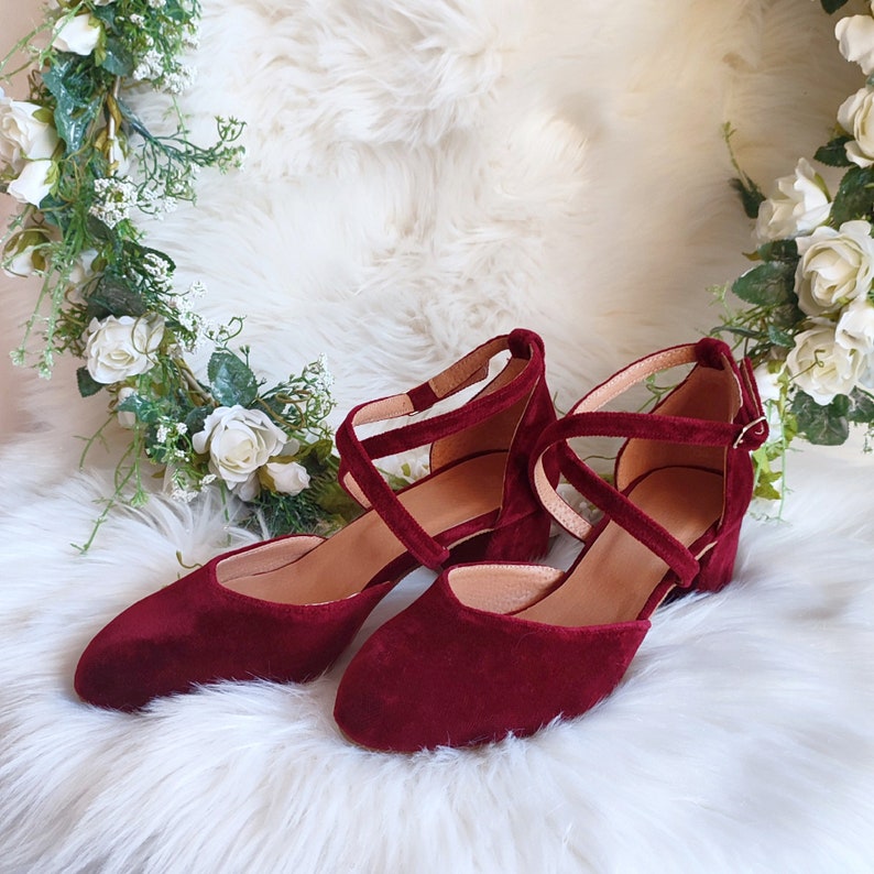 May include: A pair of burgundy velvet heeled shoes with criss-cross straps and a buckle closure.