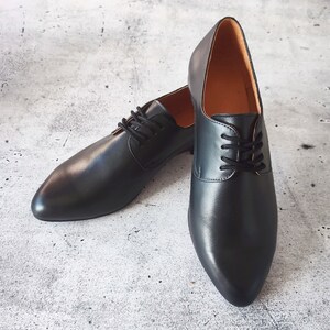 May include: A pair of black leather dress shoes with a classic lace-up design. The shoes have a pointed toe and a smooth, polished finish. The interior lining is a light brown color.