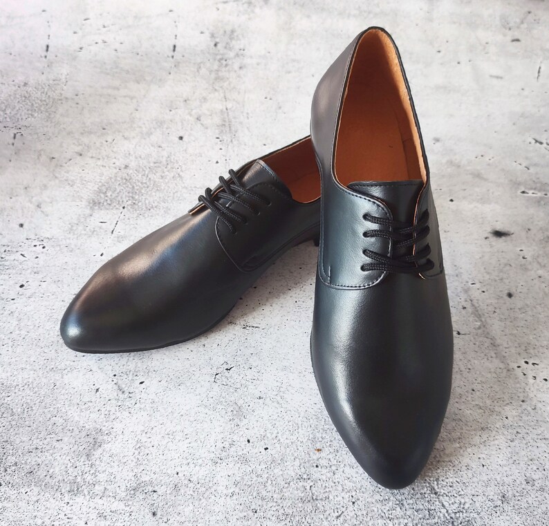 May include: A pair of black leather dress shoes with a classic lace-up design. The shoes have a pointed toe and a smooth, polished finish. The interior lining is a light brown color.
