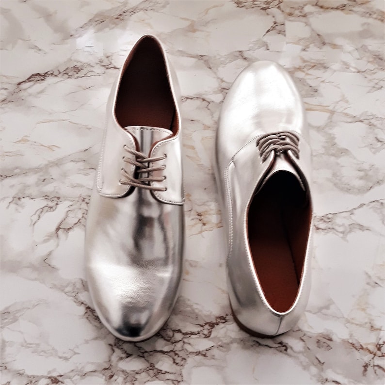 May include: A pair of silver leather lace-up shoes with a pointed toe.