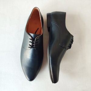 May include: A pair of black leather dress shoes with a pointed toe and lace-up closure. The shoes have a low heel and a smooth, polished finish. The interior lining is a light brown color.