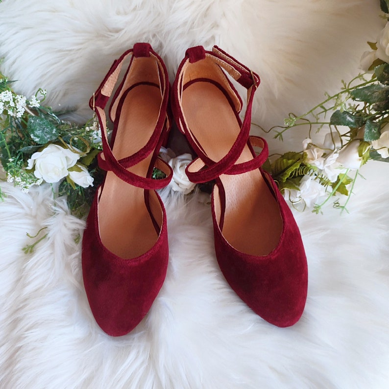 May include: A pair of burgundy velvet heeled shoes with criss-cross straps. The shoes have a pointed toe and a low heel.