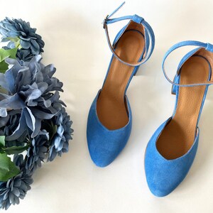 May include: A pair of blue suede heeled shoes with ankle straps. The shoes have a pointed toe and a block heel.